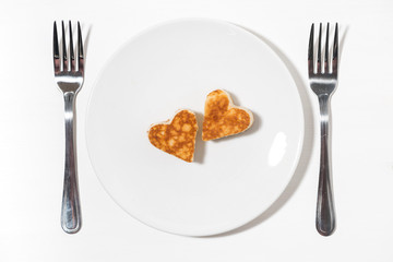 plate of pancakes in the shape of heart and two forks on white background, top view