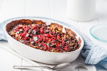 Baked oatmeal with berries and chocolate in a white dish.