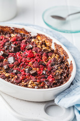 Baked oatmeal with berries and chocolate in a white dish.