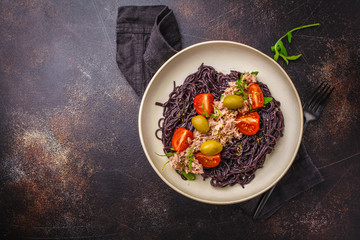Black rice pasta with tuna, tomatoes and olives in a white plate, top view.