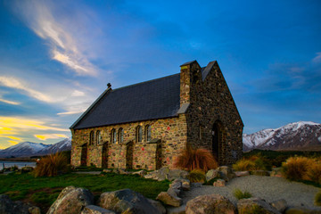 Fototapeta premium Scenic landscape view of tourist popular attraction Church of the Good Shepherd by lake Tekapo, South Island, New Zealand. Sunset colours, snow covered mountains on background. New Zealand landmarks.