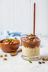 Overnight oatmeal with milk and chocolate mousse in glass on a white background.