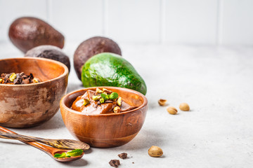 Avocado chocolate mousse with pistachios in wooden bowl on white background.