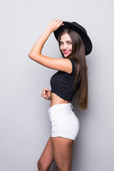 Young brunette woman wearing summer clothes holding her black hat isolated on grey background