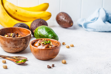 Avocado chocolate mousse with banana and pistachios in wooden bowl on white background.
