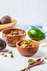 Avocado chocolate mousse with pistachios in wooden bowl on white background.