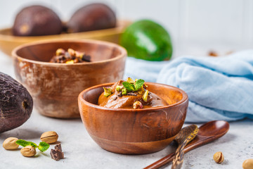 Avocado chocolate mousse with pistachios in wooden bowl on white background.