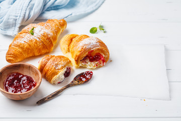 Croissants with berry jam on white wooden background.