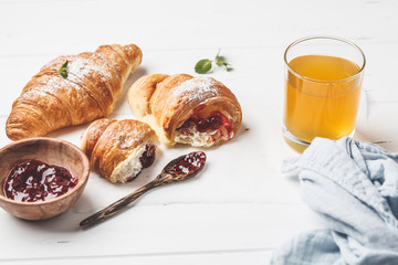 Croissants with berry jam on white wooden background.