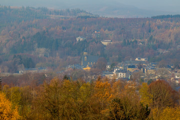 St Gengoul church with mist and surrounded by trees with yellow autumn leaves in the village of Vielsalm view from the hill Bec du Corbeau on a cold autumn day in the Belgian Ardennes