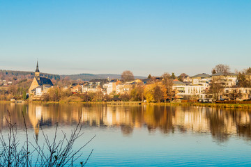 beautiful view of the village of Vielsalm and its St Gengoul church with a blue sky and the Doyards lake with a amazing reflection in the water on a wonderful cold winter day in the Belgian Ardennes