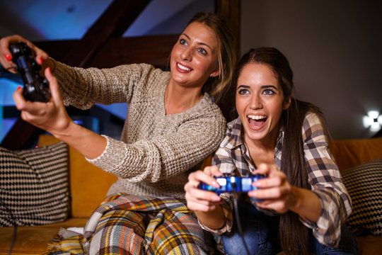 Two female best friends sitting at home on pleasant evening and playing games on console.They challenge each other to win.
