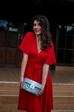 Fashion women accessories. Fashionable girl in red drees holding leather snakeskin python bag, Elegant outfit. Elegant model near the expensive villa. Place for text or your logo. Top view.