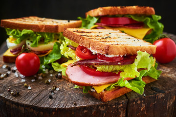 Homemade sandwich with ham, lettuce, cheese and tomato on a wooden background