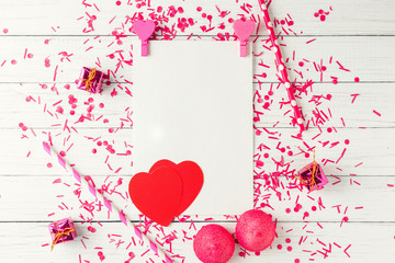 Epty white paper sheet with confetti and valentines decorations on a white wooden background, top view. Holiday composition