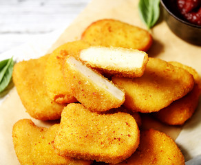 Fried chicken nuggets with ketchup and basil leaves on a white background.