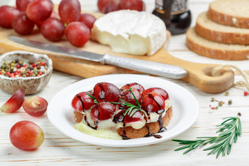 Bruschetta of Camembert or brie cheese with red grapes, rosemary and balsamic. crostini. Gourmet wine snacks for foodies. Italian antipasti. Selective focus