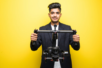 Professional indian man videographer with gimball video slr isolated on yellow background © dianagrytsku