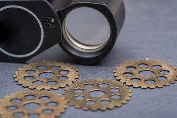 Loupe, magnifying glass and old vintage antique hour metal gears, cogwheels on natural stone background.