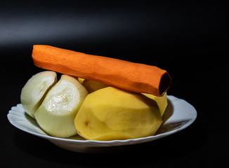 Raw carrot potatoes and onions close-up on a plate