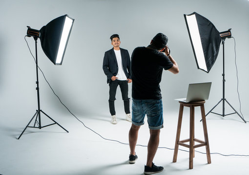 Photographer shooting model in studio with softboxes. Young man photographer shooting male model and show example on laptop in studio. Working proces.
