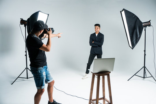 Professional photo shooting at the studio: young man model is smiling and posing the photographer is taking pictures with a digital camera