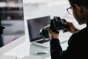 Young cheerful photographer man use photocamera while working in his office