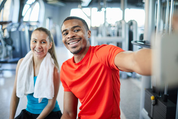 Fototapeta na wymiar Happy young intercultural man and woman making selfie in fitness center at break after training