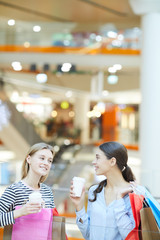 Two young restful shoppers with bags having drinks and discussing what to do next in the mall