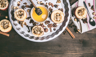 baked apples with nuts and honey on a round baking tray on a wooden background, top view