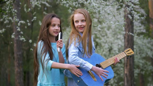 two girlfriends having fun outdoors. Young people enjoying a spring day in the forest. small girls playing guitar and sing songs.
