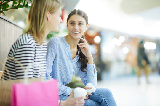 Two restful girls chatting in large modern mall while having break between shopping