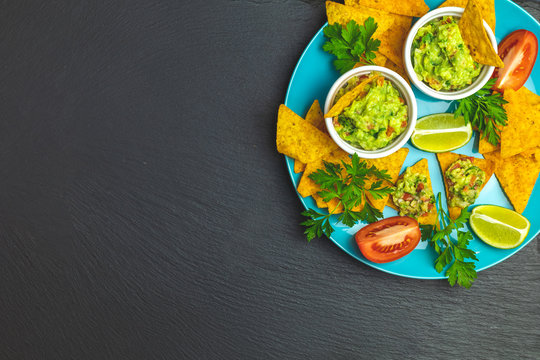 Guacamole and nachos with ingredients on the background of a black stone board
