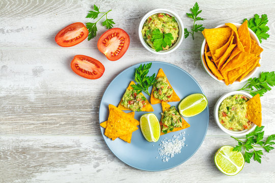 Guacamole and nachos with ingredients on the background of a light gray wooden board.