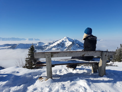 Frau macht Pause auf Bank und blickt in schneebedeckte Berglandschaft
