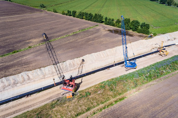 Pipelinebau - Kräne heben Stahlrohre für eine Gaspipeline vorsichtig in die neue Trasse, Luftbild
