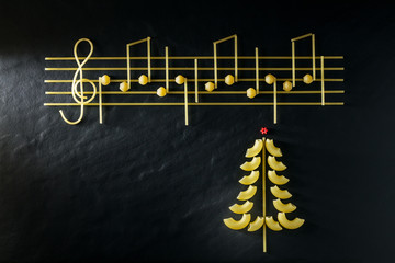 Musical Christmas Italian pasta in the form of notes and a Christmas tree, isolated on a black textural background.