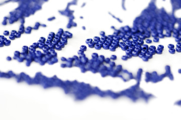 Dark blue seed beads scattered on a white surface close up