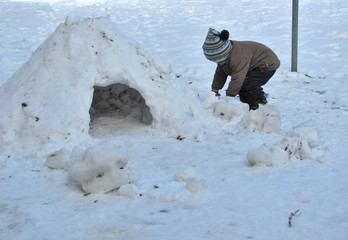 Kind spielt im Schnee und baut Iglu