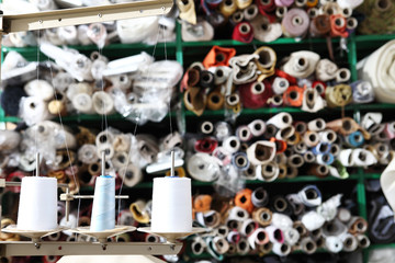 shelves with rolls of colored fabrics and spools of sewing thread in the foreground