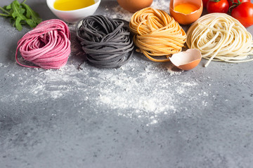 Ingredient of traditional mediterranean cuisine. Raw colored pasta noodle, olive oil, tomatoes and arugula. Copy space for text. Food background.