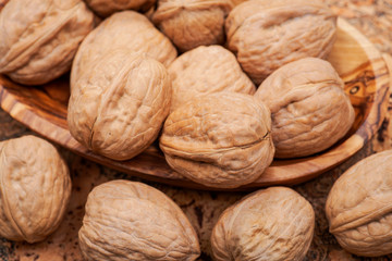Brown premium raw organic walnuts in wooden bowl on cork background.