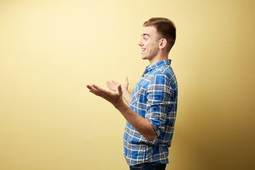 Surprised guy dressed in a plaid shirt and jeans stands next to yellow wall in the studio