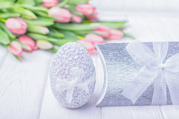 Silver Easter egg, gift box and pink tulips on a white wooden background