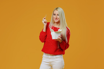 Bright blond woman eating asian fast food from takeaway box with chop sticks, Wok noodles concept