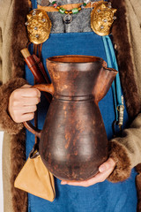 woman in medieval clothes holds a clay pot in her hands