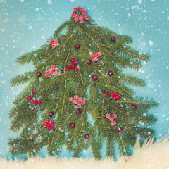 Christmas tree maked of spruce branch decorated red holly berries on blue. Top view. Xmas...