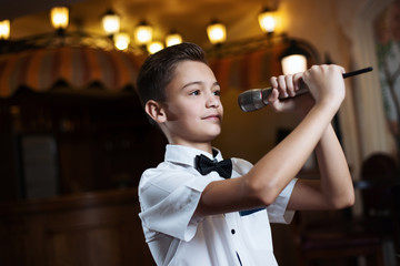 Boy in a white shirt singing into the microphone in a restaurant. baby karaoke.