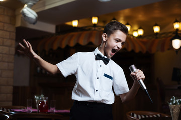 Boy in a white shirt singing into the microphone in a restaurant. baby karaoke.