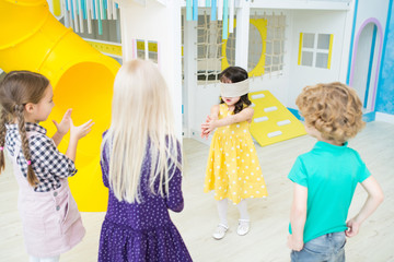 Asian little girl in yellow dress walking over games room and catching up friends while playing tag...